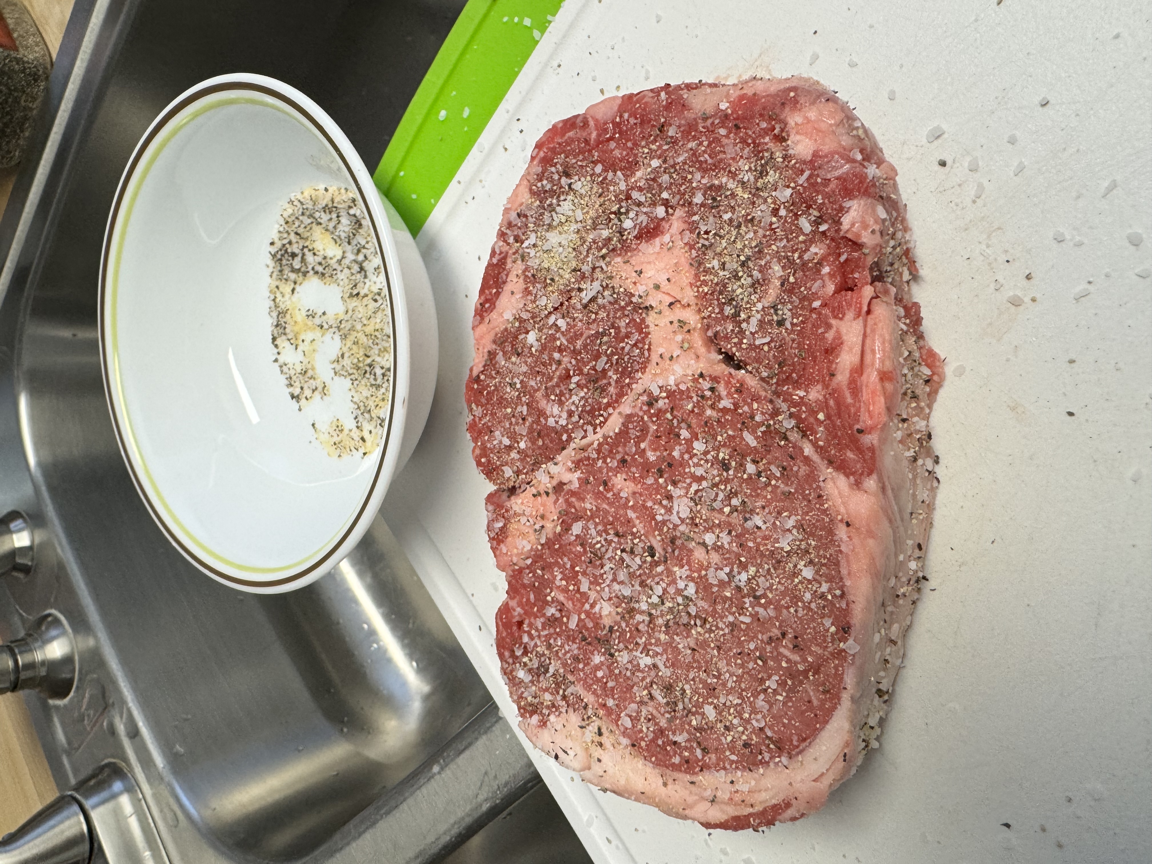 Steak being seasoned with salt, pepper, and garlic powder.